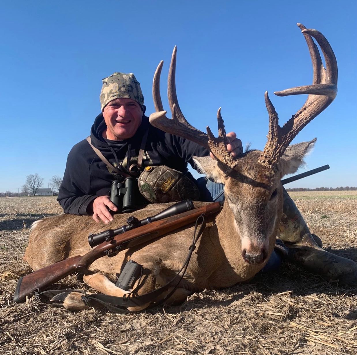 Ronnie Adams posing with a large deer and rifle in an open field