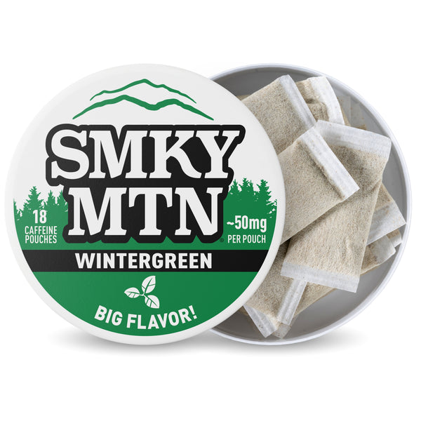 A round tin of Smky Mountain Wintergreen caffeine pouches, with the white and green lid leaning against the open can. The lid features the brand name 'SMKY MTN' in bold black letters with green mountain and pine graphics.