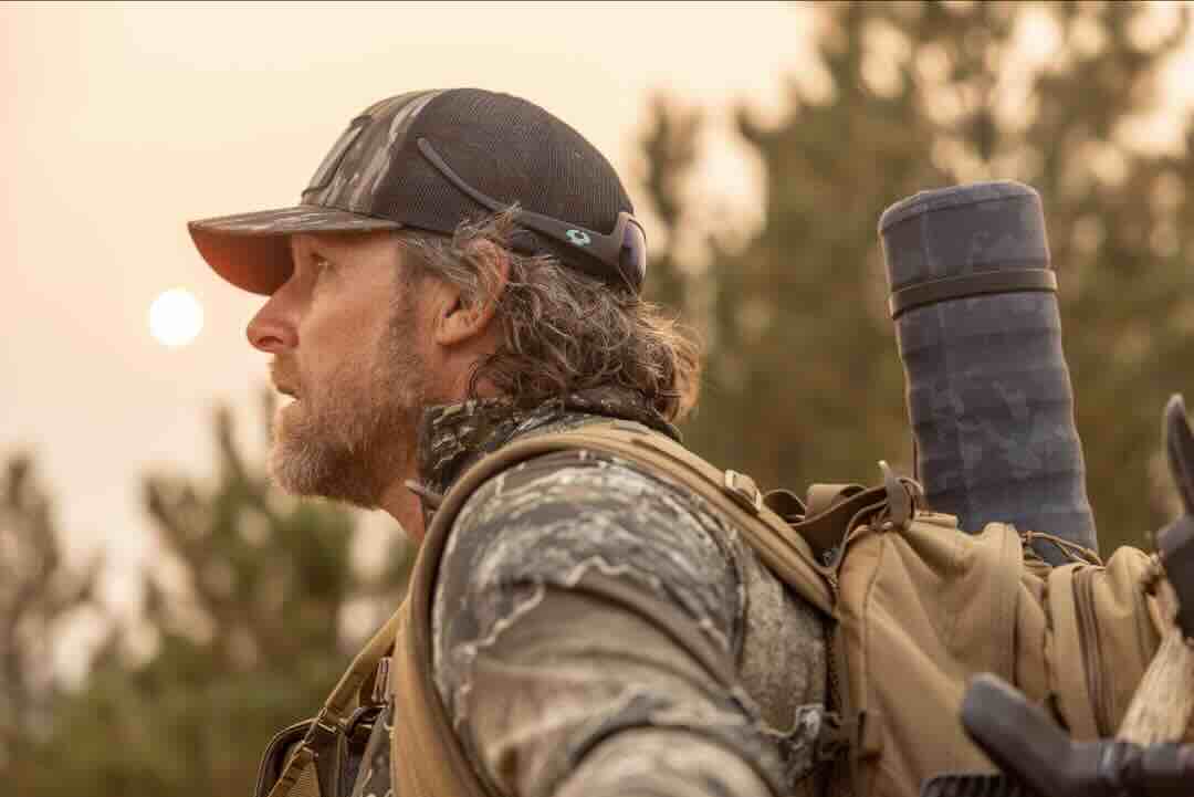 Matt Duff from Major League Bowhunter in camouflage gear with a backpack and binoculars in a forest setting