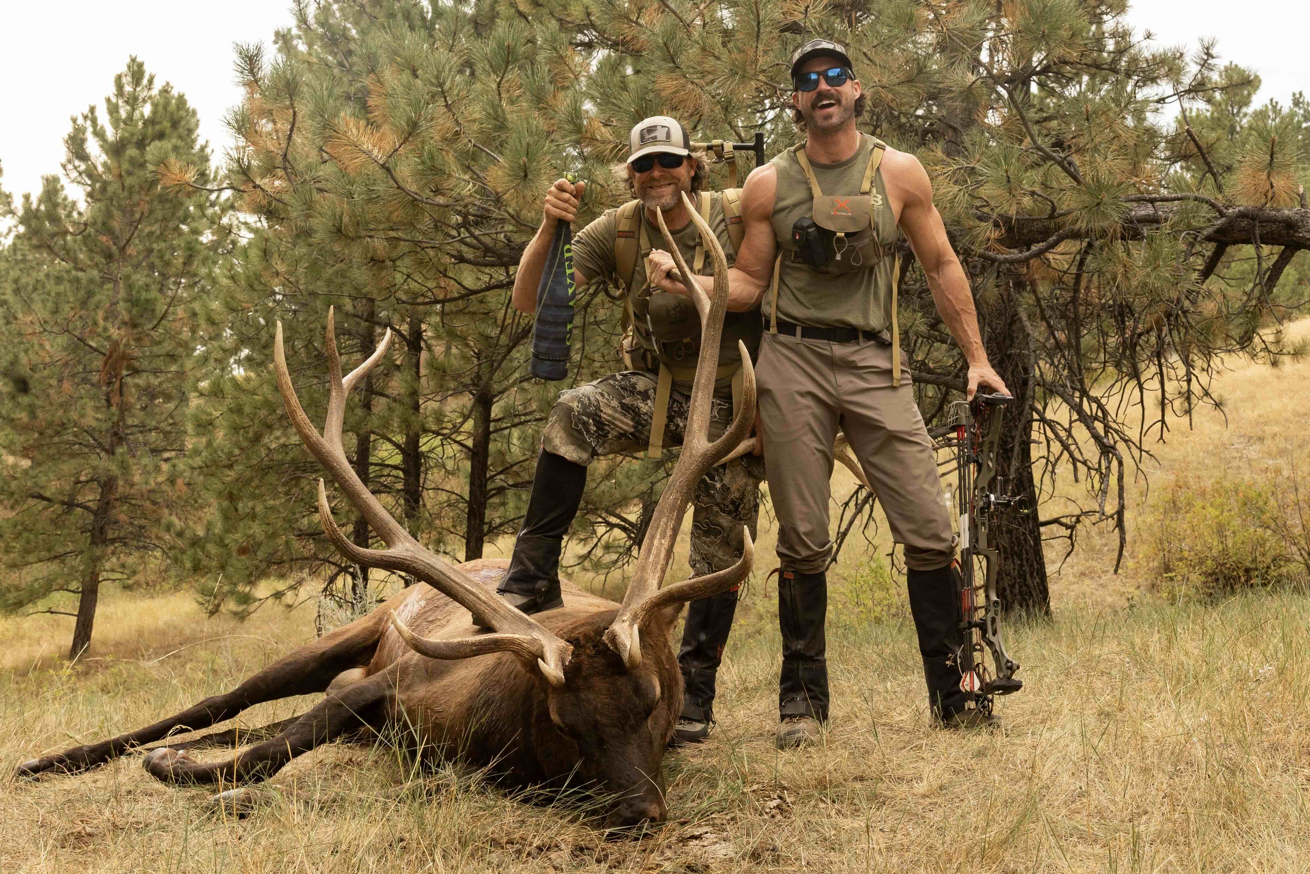 Matt Duff and Riley Green with a large elk in a forested area