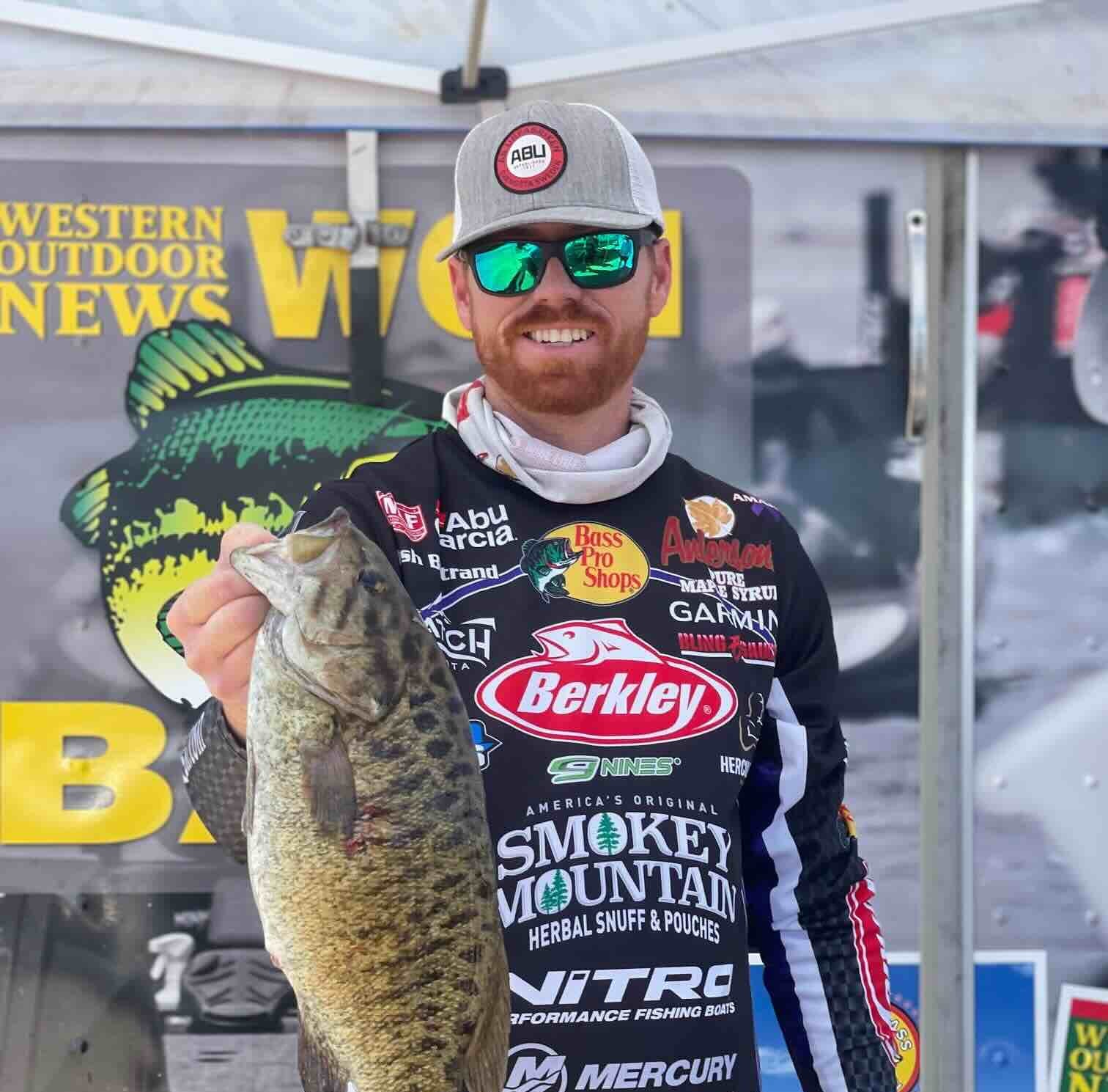 Josh Bertrand holding a large fish with outdoor and fishing brand logos in the background