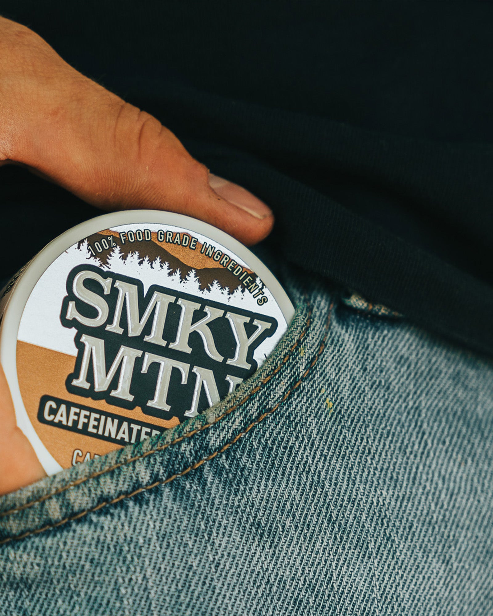 A man pulling a can of smokey mountain caramel coffee flavored caffeinated pouches out of the front pocket of his blue jeans.