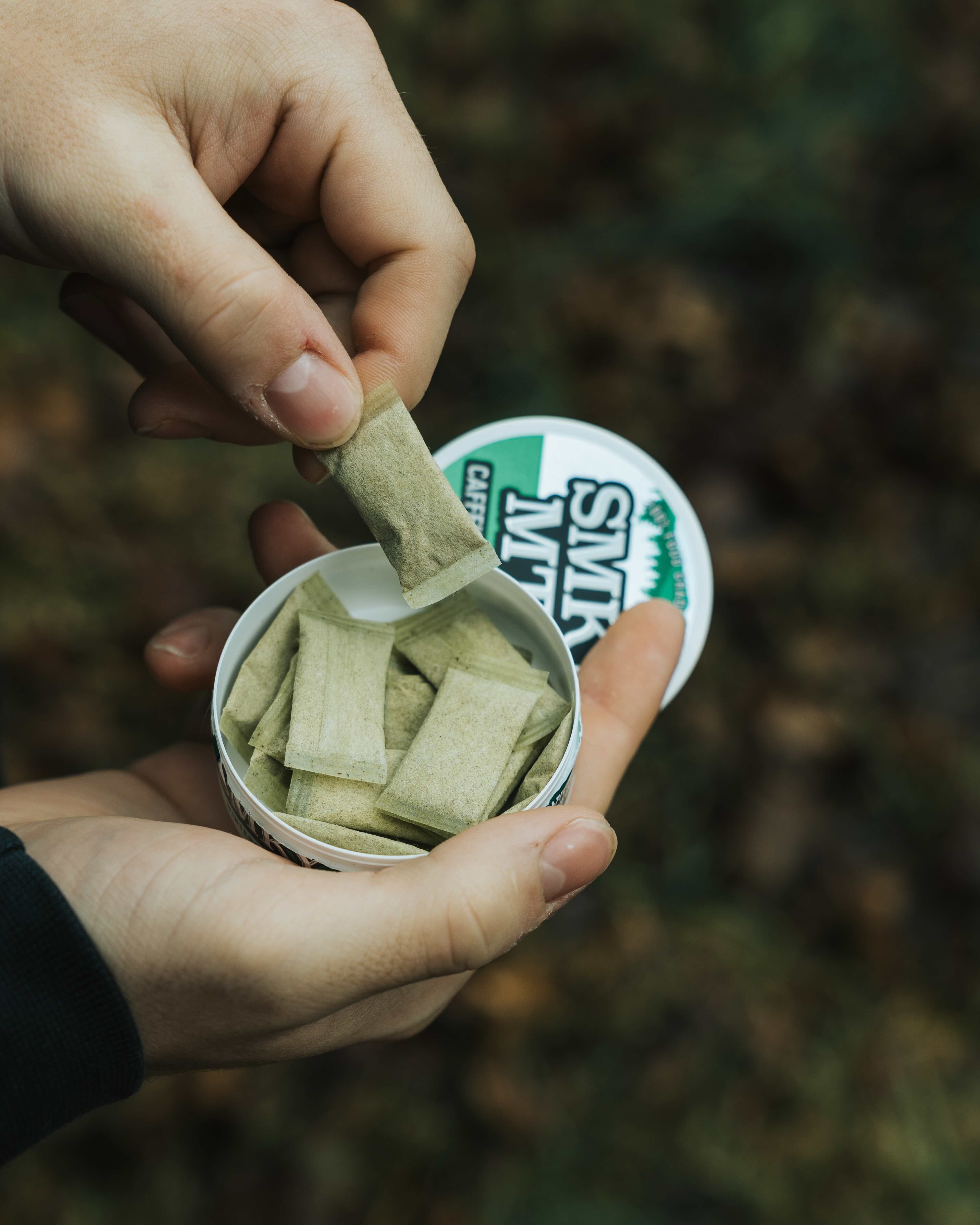 hand grabbing a smokey mountain caffeine pouch from the can with a woodsy background