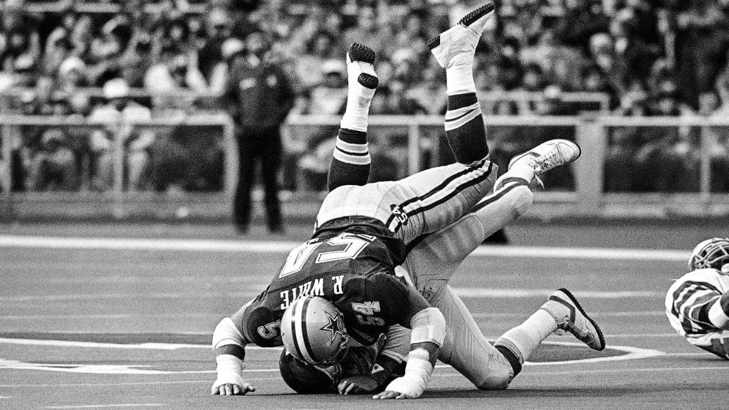 Black and white photo of a football player being tackled on the field by Randy White